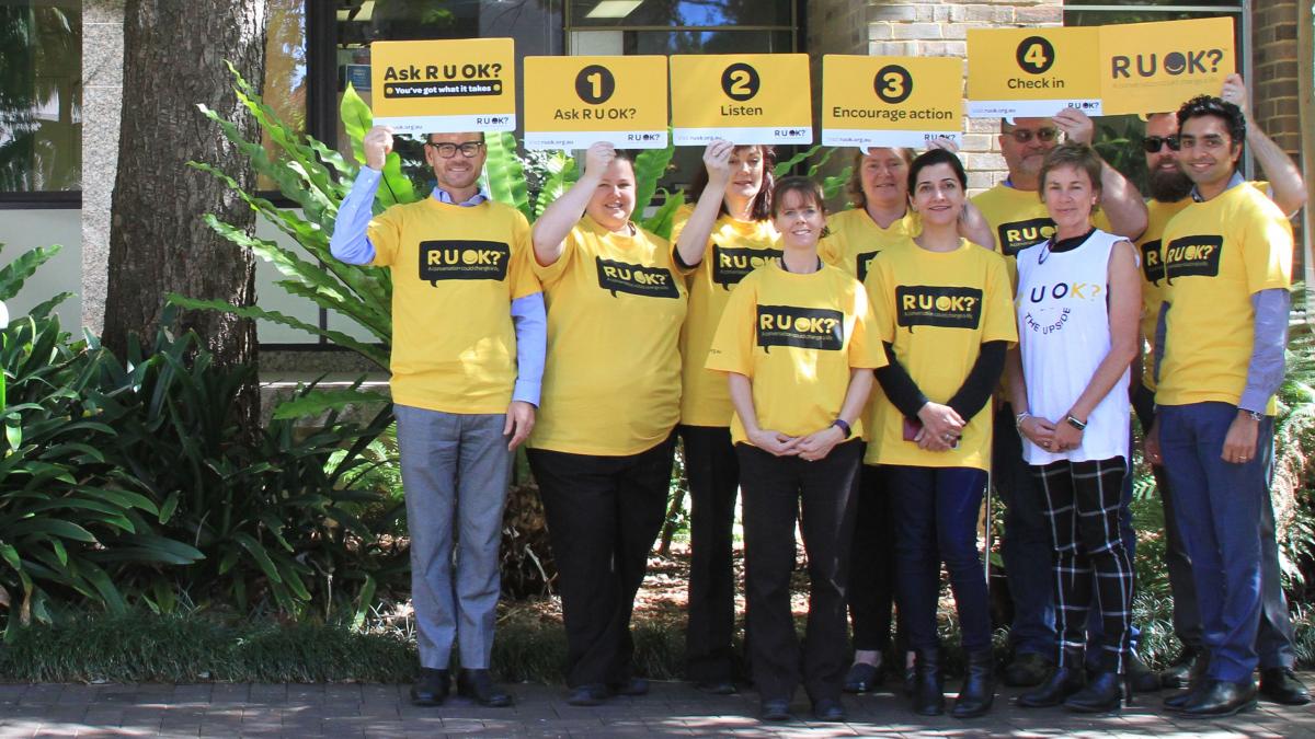 Iamge of group of people holding up signs sayng R U OK?