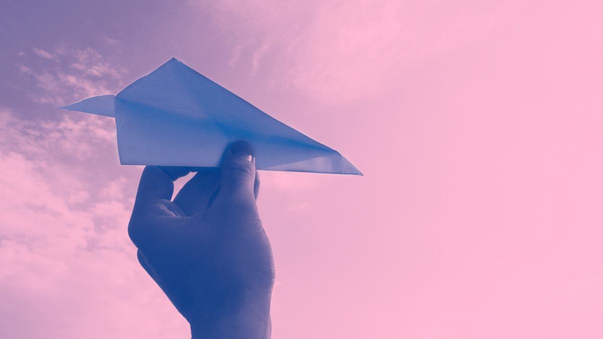 Blue hand throwing paper airplane in a pink sky
