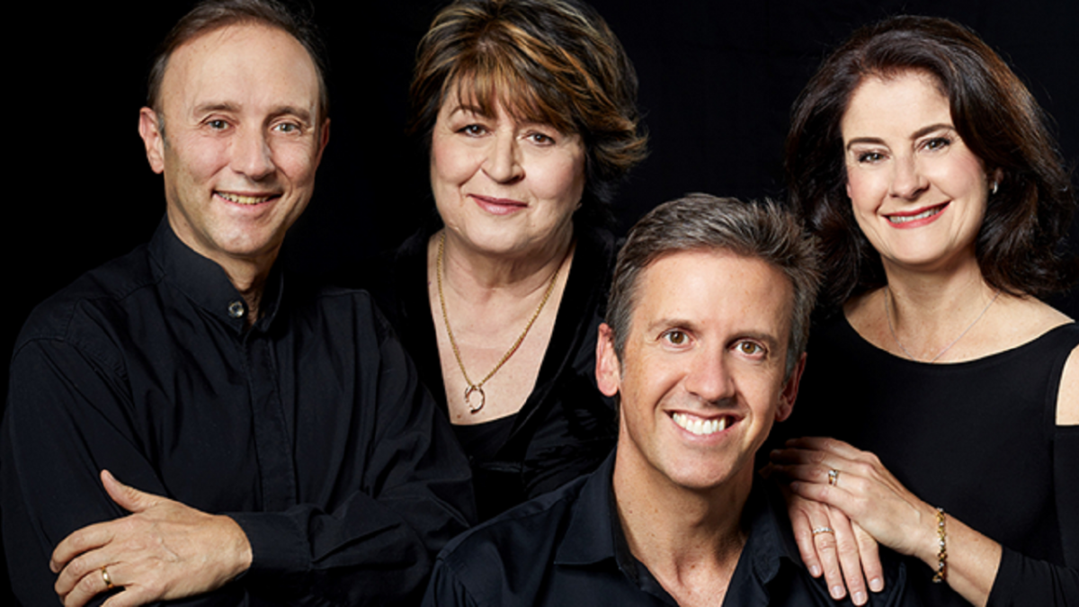 Four people wearing black clothing. They are smiling and standing close together.